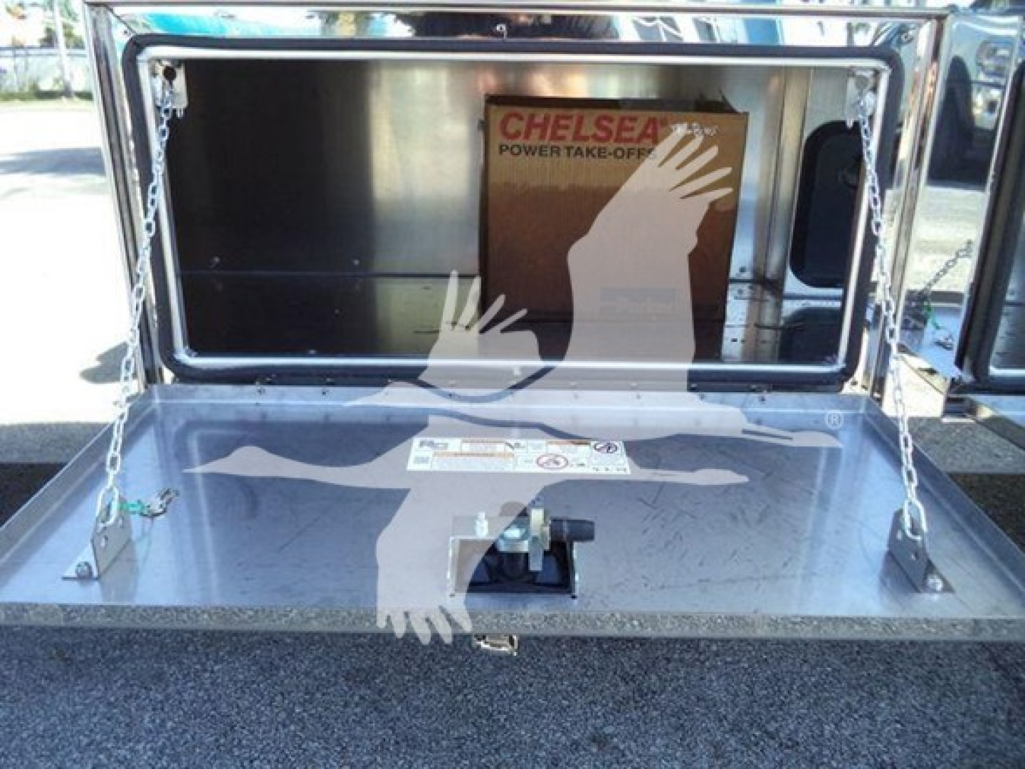 Kenworth rollback bed with chrome toolbox and raised lid showing chelsea power take-off label, metallic surface with chains and latches.