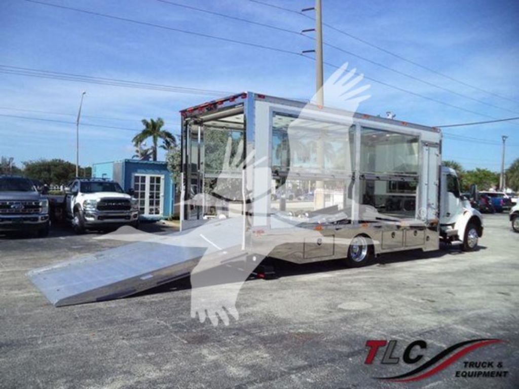 Kenworth T280 rollback truck with a large glass-walled cargo area and a deployed aluminum ramp, chrome finish, used in a dealership lot.