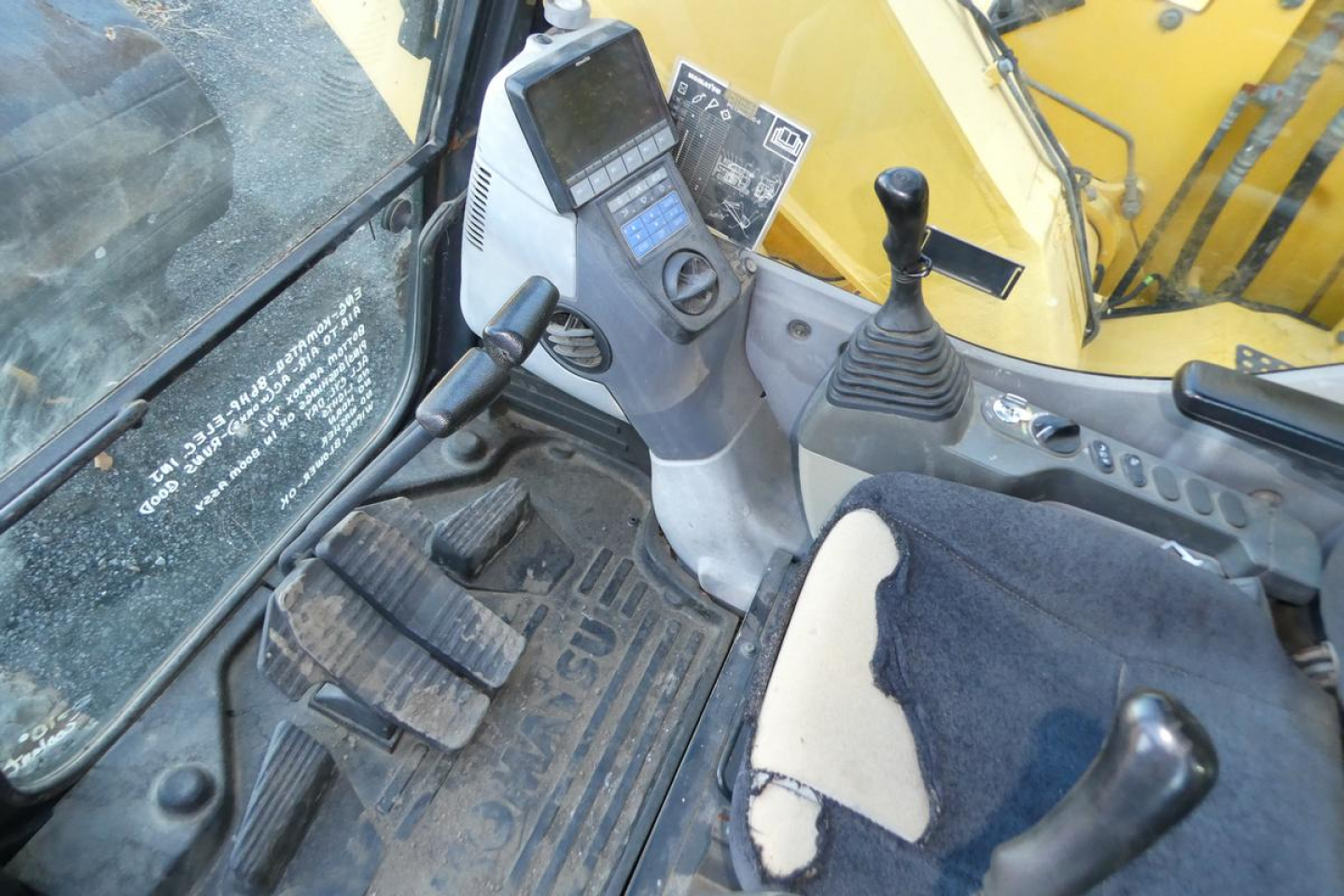 Komatsu PC128US-8 cab interior showing joystick controls and dashboard with digital display.