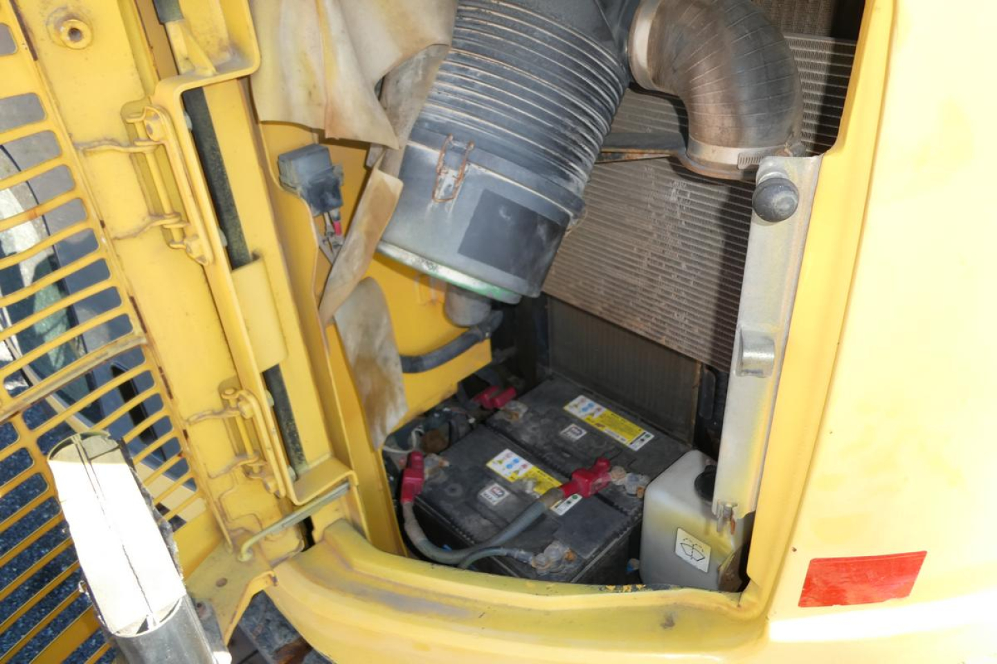 Engine bay of a Komatsu PC128US-8 excavator showing battery and air intake hose connections.