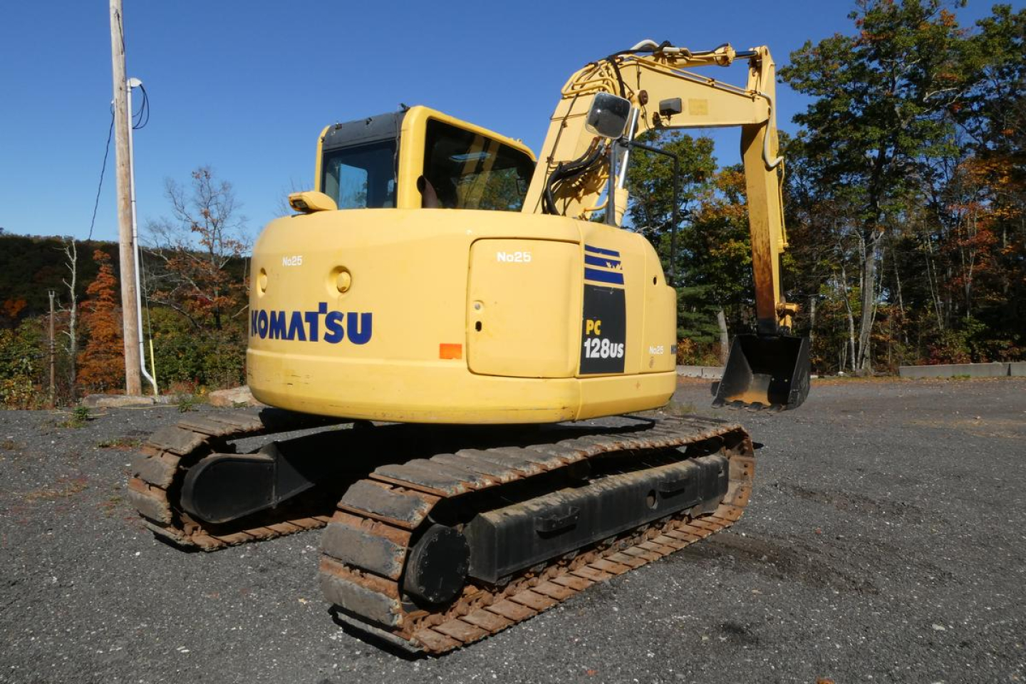 Komatsu PC128US-8 excavator with yellow body and black tracks, viewed side profile in an outdoor lot.