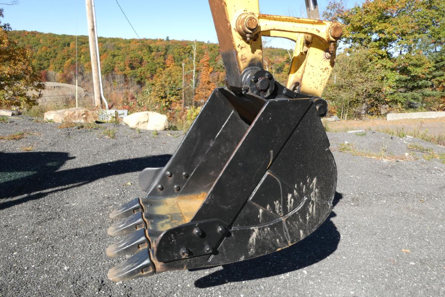 Excavator bucket attached to hydraulic arm of a Komatsu PC128US-8, black metal bucket with teeth ready for digging.