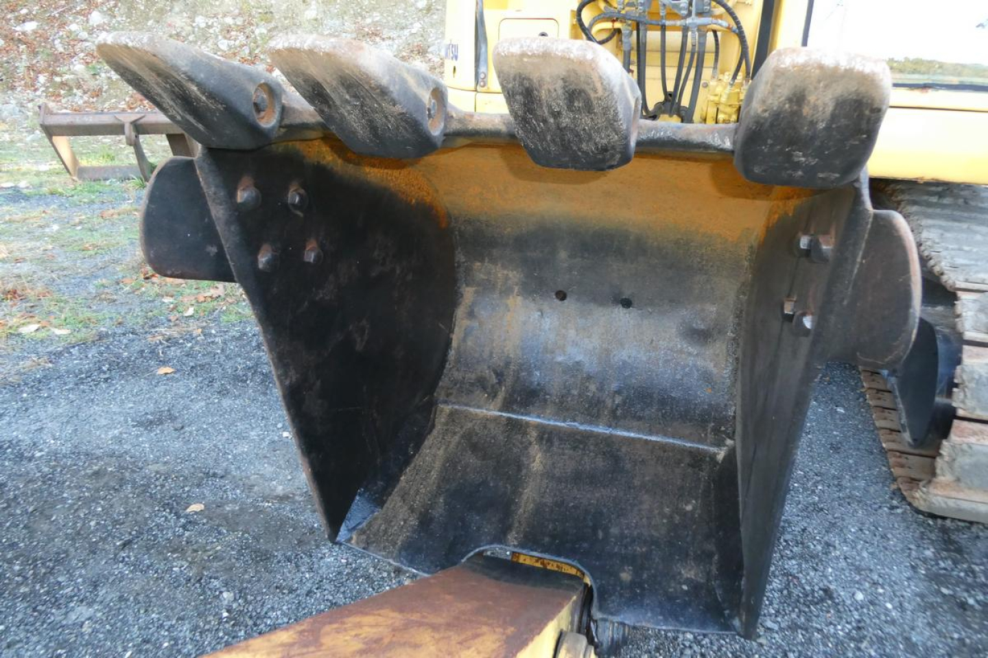Excavator bucket attachment on a Komatsu PC128US-8 showing wear and dirt, with hydraulic arms in background.