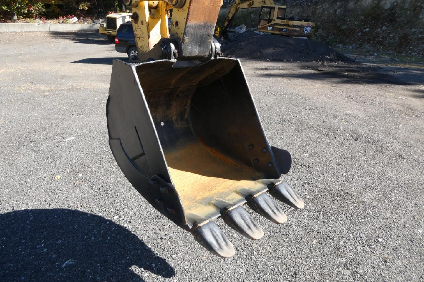 Excavator bucket attachment on a Komatsu PC128US-8 showing medium-duty steel bucket with teeth and hydraulic coupler.