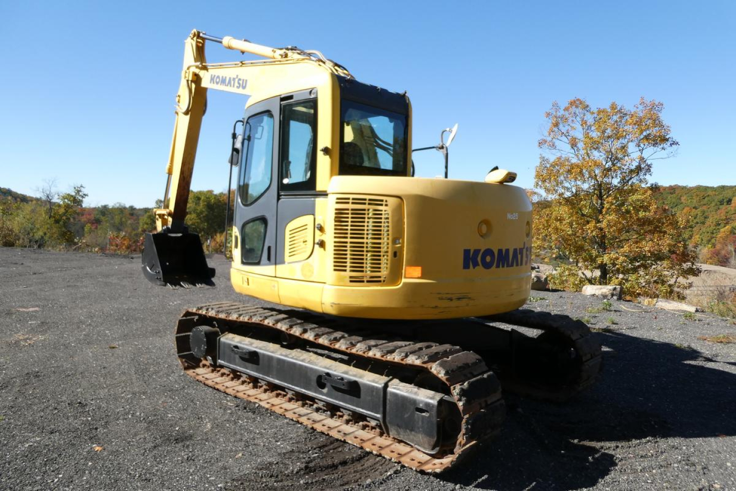 Komatsu PC128US-8 excavator side view showing Komatsu branding, yellow body, track undercarriage, hydraulic arm and bucket.
