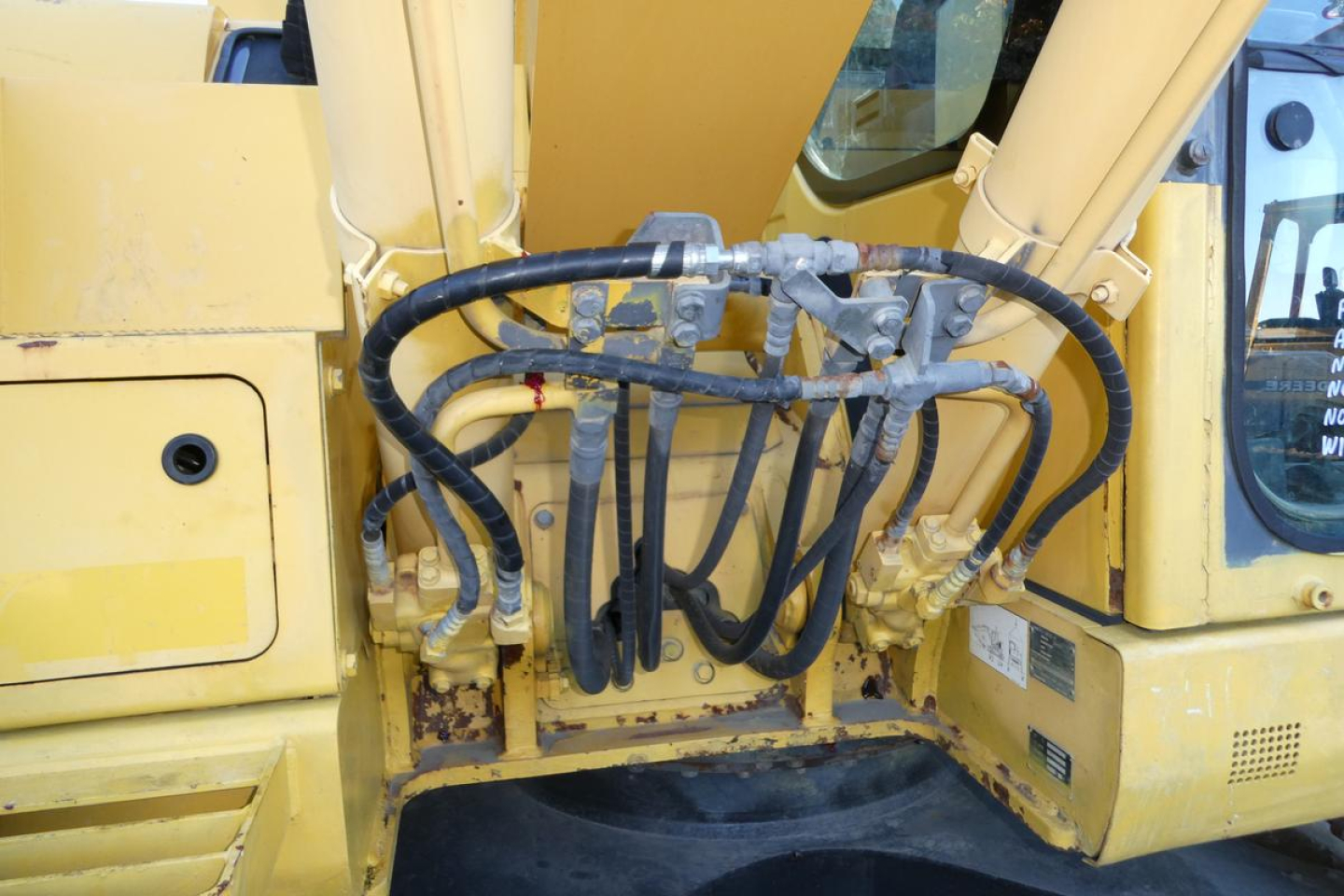 Komatsu PC128US-8 excavator hydraulic hoses and cab area, showing multiple high-pressure hoses connected to a central control manifold.
