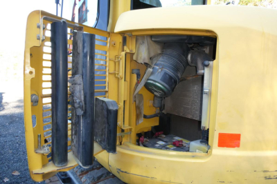 Komatsu PC128US-8 excavator engine bay showing radiator, air filter housing, and hydraulic fluid components.