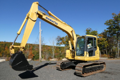 Komatsu PC128US-8 excavator with yellow body and black tracks, hydraulic arm extended with bucket, machine name 'KOMATSU' on boom.
