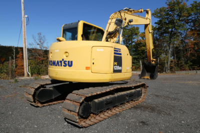 Komatsu PC128US-8 excavator with yellow body and black tracks, viewed side profile in an outdoor lot.