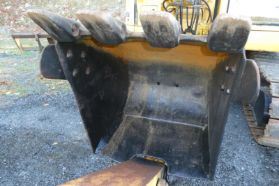 Excavator bucket attachment on a Komatsu PC128US-8 showing wear and dirt, with hydraulic arms in background.