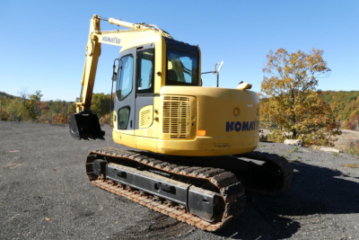 Komatsu PC128US-8 excavator side view showing Komatsu branding, yellow body, track undercarriage, hydraulic arm and bucket.