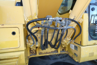 Komatsu PC128US-8 excavator hydraulic hoses and cab area, showing multiple high-pressure hoses connected to a central control manifold.