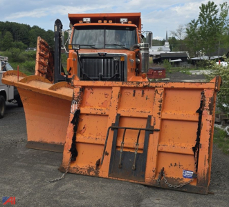 Orange Western Star 4900 SF dump truck with large front snow plow attachment viewed head-on in a lot.