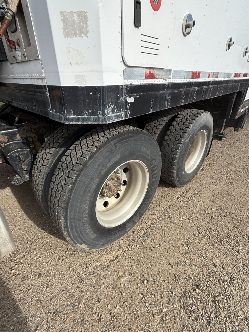 Dual rear axles of a Volvo truck with off-white wheels and visible tire treads showing on a gravel surface.