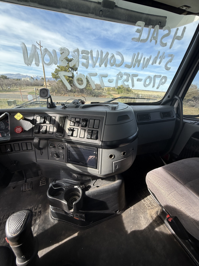 Truck cab interior view showing dashboard with multiple switches, steering column, and cup holder.