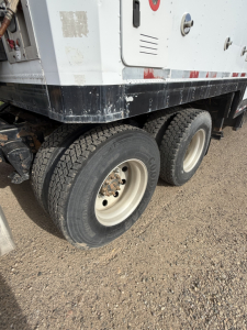 Dual rear axles of a Volvo truck with off-white wheels and visible tire treads showing on a gravel surface.