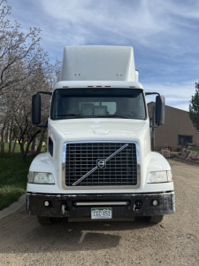 Front view of a white 2005 Volvo VNL64T300 truck showing large grille, Volvo emblem, rectangular headlights, bumper, and hood between side mirrors.