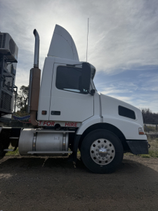 Truck cab side view of a 2005 Volvo VNL64T300 with white exterior, tall sleeper, large exhaust stack, and front wheel visible.