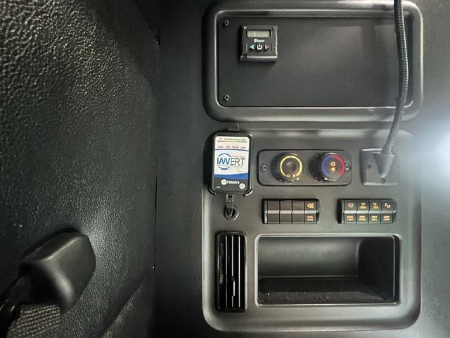 Cab area of a Freightliner Cascadia 126 truck showing dashboard panel with switches, two circular gauges, an In-Verb water separator? sticker, and a small open storage compartment.