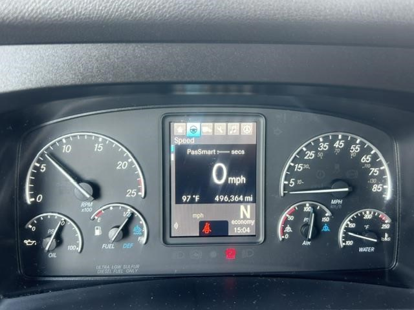 Dashboard cluster of Freightliner Cascadia showing digital display with 0 mph and various gauges. Center display shows speed, odometer 496,364 mi, 97°F outside temp. Left gauges include tachometer and fuel, right gauges include air pressur