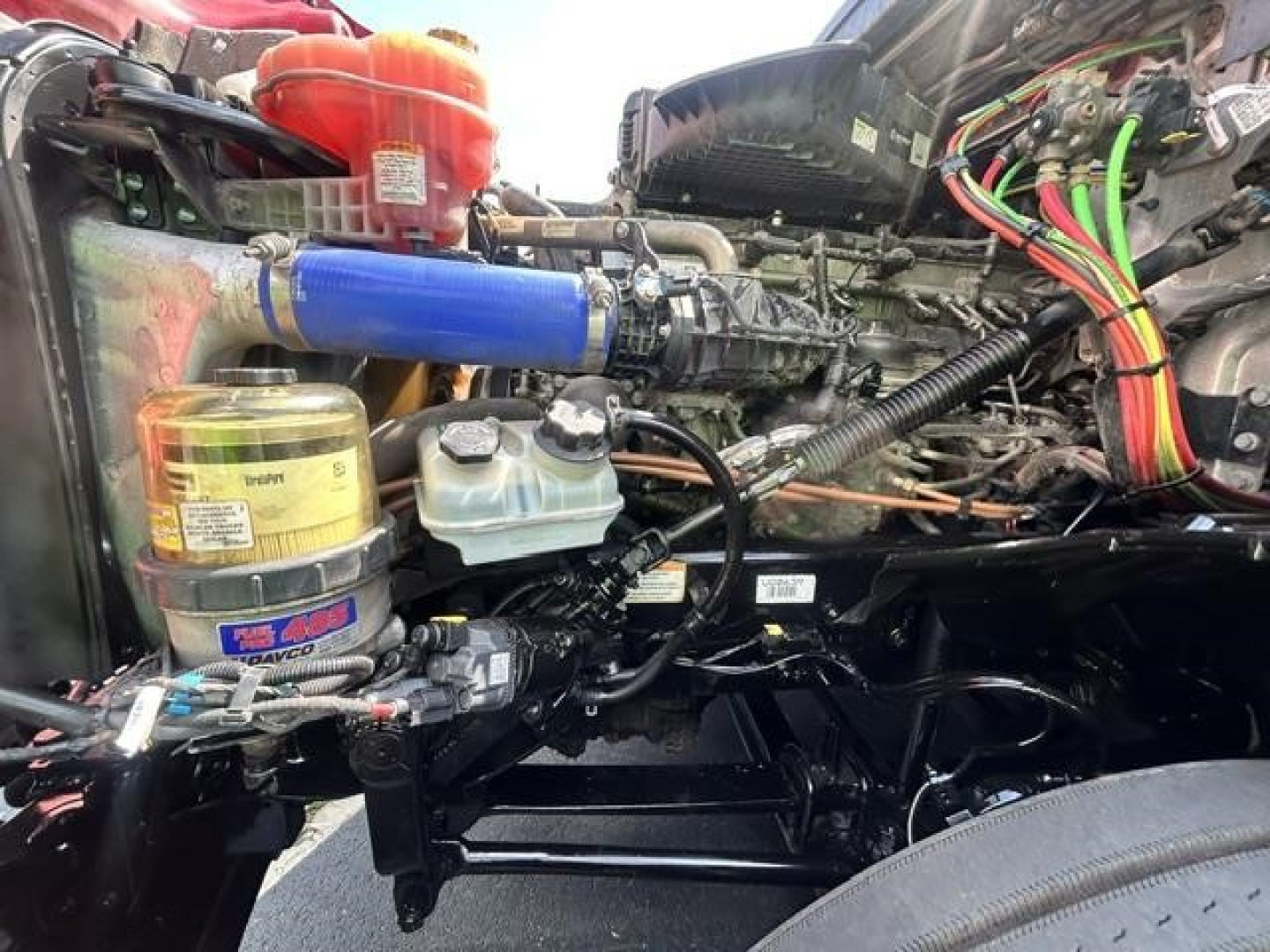 Freightliner Cascadia engine bay showing blue intercooler hose, coolant reservoir, and assorted hoses and wiring harnesses.