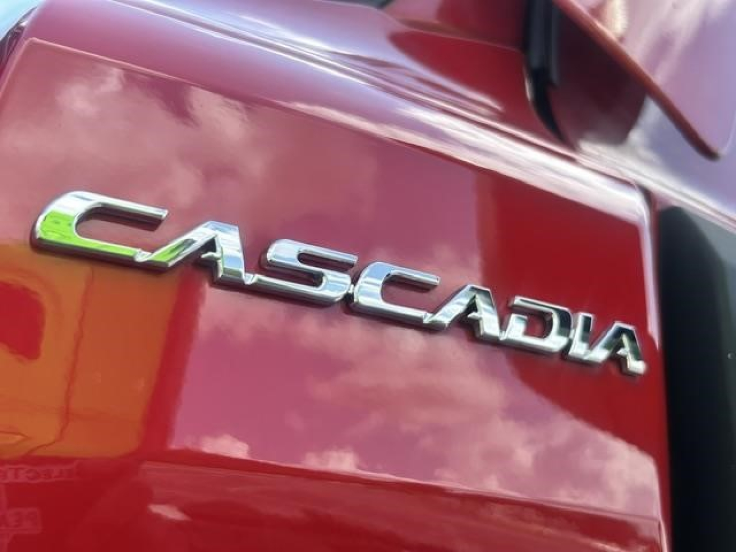 Freightliner Cascadia emblem on red truck side panel showing 'CASCADIA' chrome lettering.