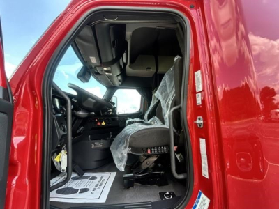 Driver’s side cab of a Freightliner Cascadia truck with the door open; interior shows the steering wheel, dashboard, and a plastic-covered seat.