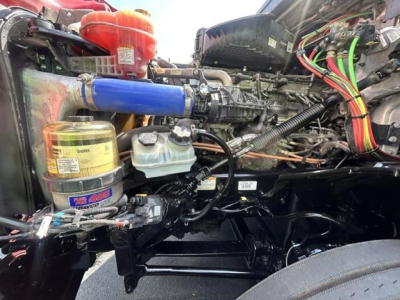Freightliner Cascadia engine bay showing blue intercooler hose, coolant reservoir, and assorted hoses and wiring harnesses.