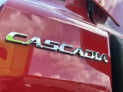 Freightliner Cascadia emblem on red truck side panel showing 'CASCADIA' chrome lettering.
