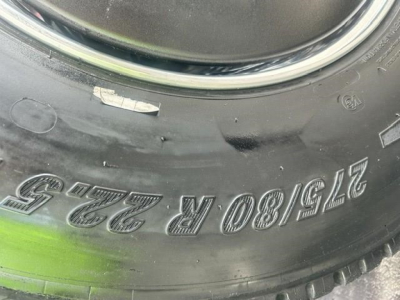 Tire sidewall with stamped numbers 275/80 R 22.5 and wheel tread; partial green paint on tire; close-up view of wheel area