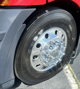 Truck wheel close-up on Freightliner Cascadia showing shiny chrome hub and black tread tire with reflective surface.