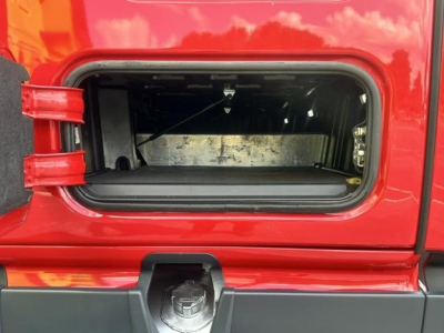 Truck cab exterior showing open storage compartment on a red Freightliner Cascadia 126 with interior metal wall and hinge area visible