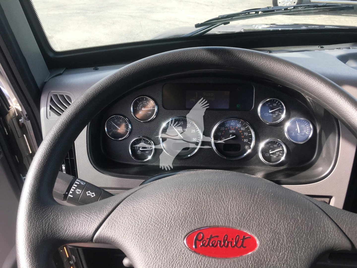 Truck cab dashboard and steering wheel with Peterbilt logo visible in center; gauge cluster and windshield visible.