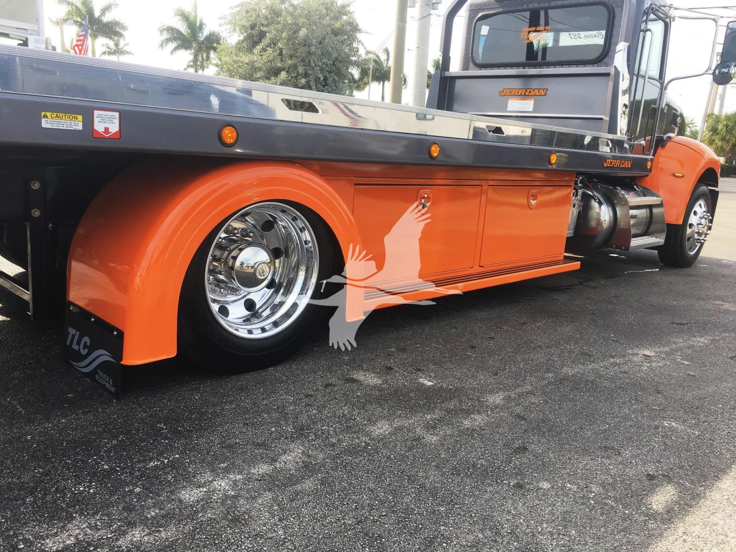 Peterbilt 337 rollback truck side view showing bright orange equipment with chrome wheel and black flatbed; visible markings include small stickers and brand logos on the side.