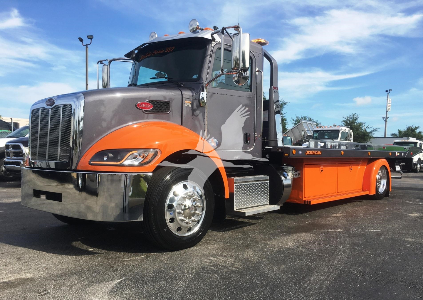 Peterbilt 337 rollback truck with gray cab and orange flatbed, front grille, chrome bumper, and side steps.