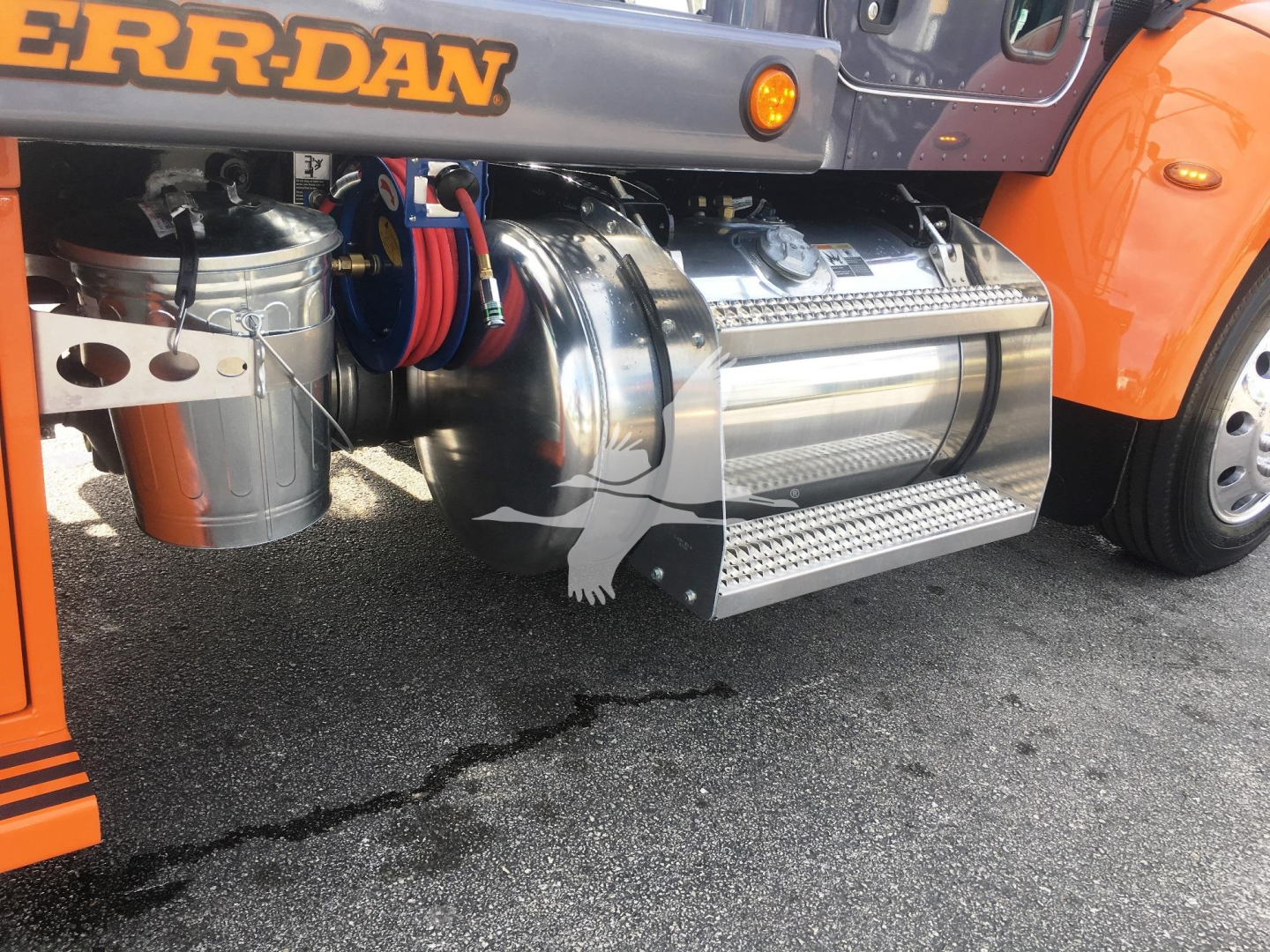 Peterbilt 337 side view showing chrome fuel tank and steps, orange body, and black chassis with hoses and wiring visible.