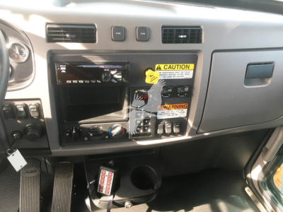 Dashboard area of a 2022 Peterbilt 337 cab showing instrument cluster space, control switches, and blank radio slot; visible labels include caution sticker and warning tag on the center panel.