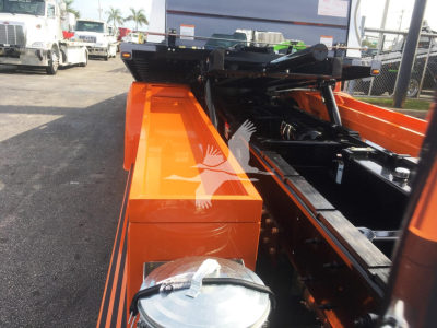 Orange Peterbilt 337 rollback bed with metal chassis and hydraulic components visible; close view of storage box and towing mechanism