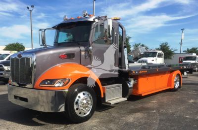 Peterbilt 337 rollback truck in service showing front grille, orange lower body and bed, chrome bumper, and large mirrors.