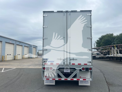 Rear view of a Vanguard VXP plate van trailer showing doors with latches and rear lights; company branding and reflective safety chevrons at bottom.