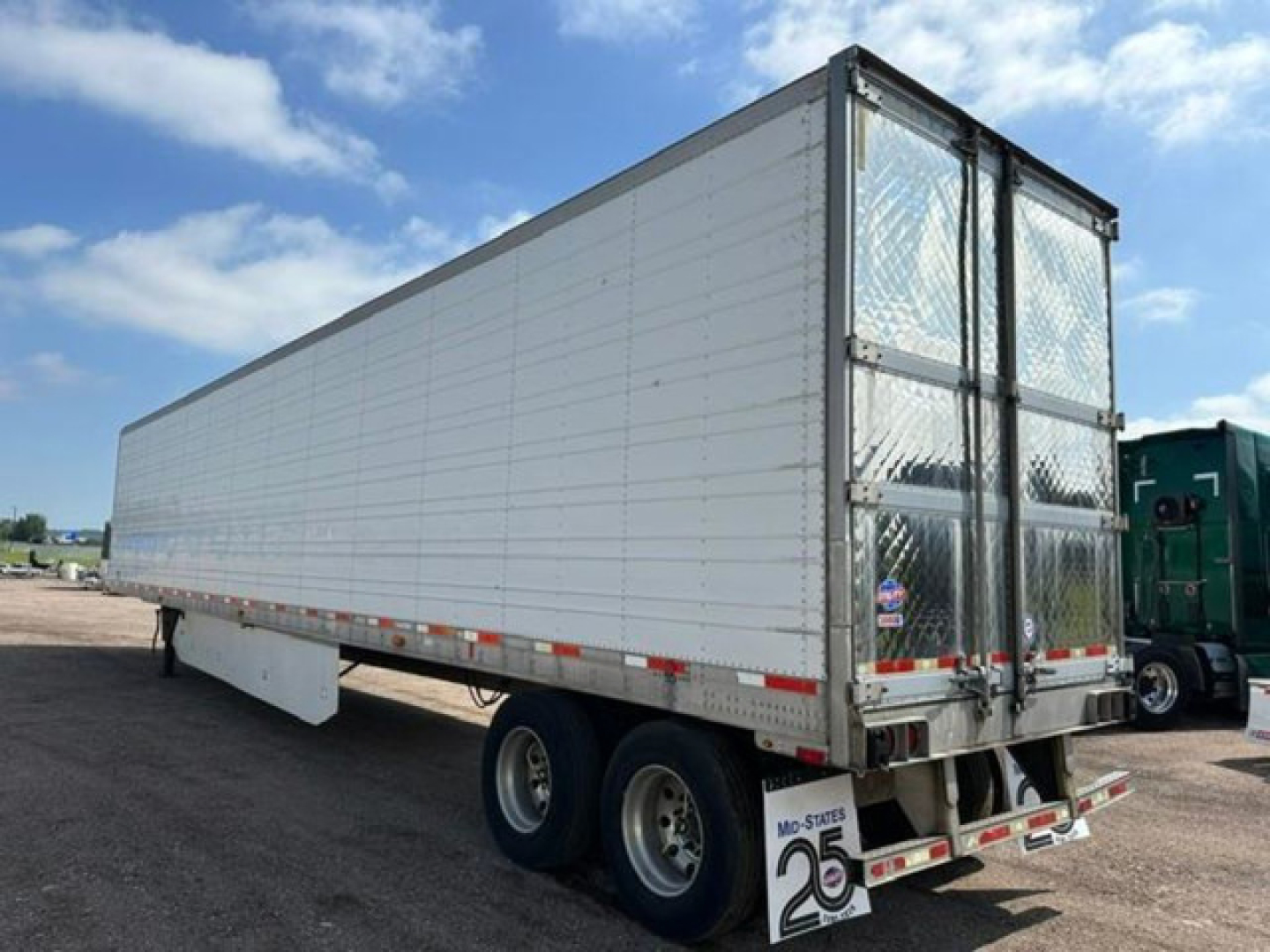 Trailer side and rear showing tandem axles, white reefer trailer, aluminum doors with lattice pattern on rear, metal framing, reflective strips.