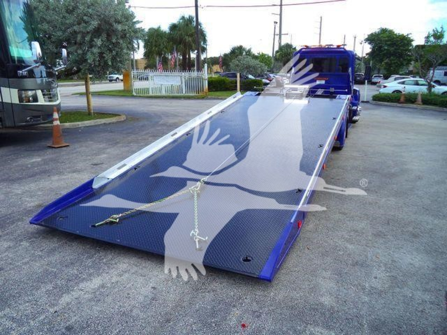 Truck bed with a blue Peterbilt rollback tilt trailer extended in a parking lot.