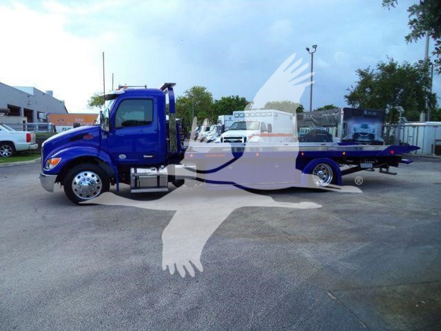 Blue Peterbilt 536 rollback truck side view showing cab and long flatbed with chrome wheels.