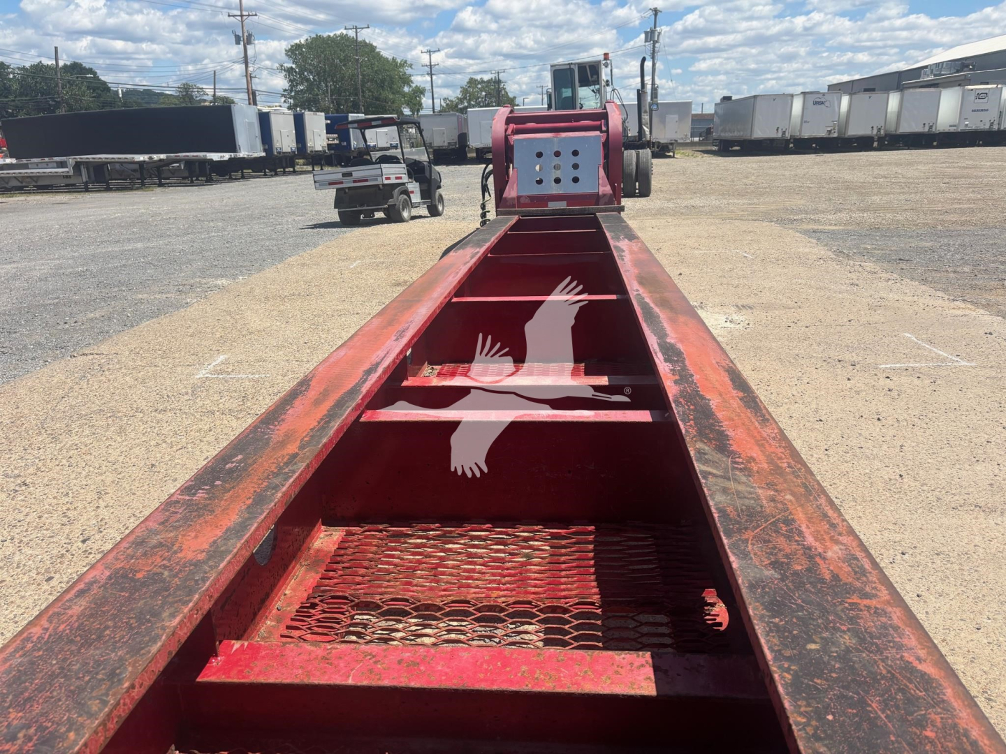 Beam-style Fontaine lowboy trailer side view showing red steel frame and grated deck with top coupler and storage areas.