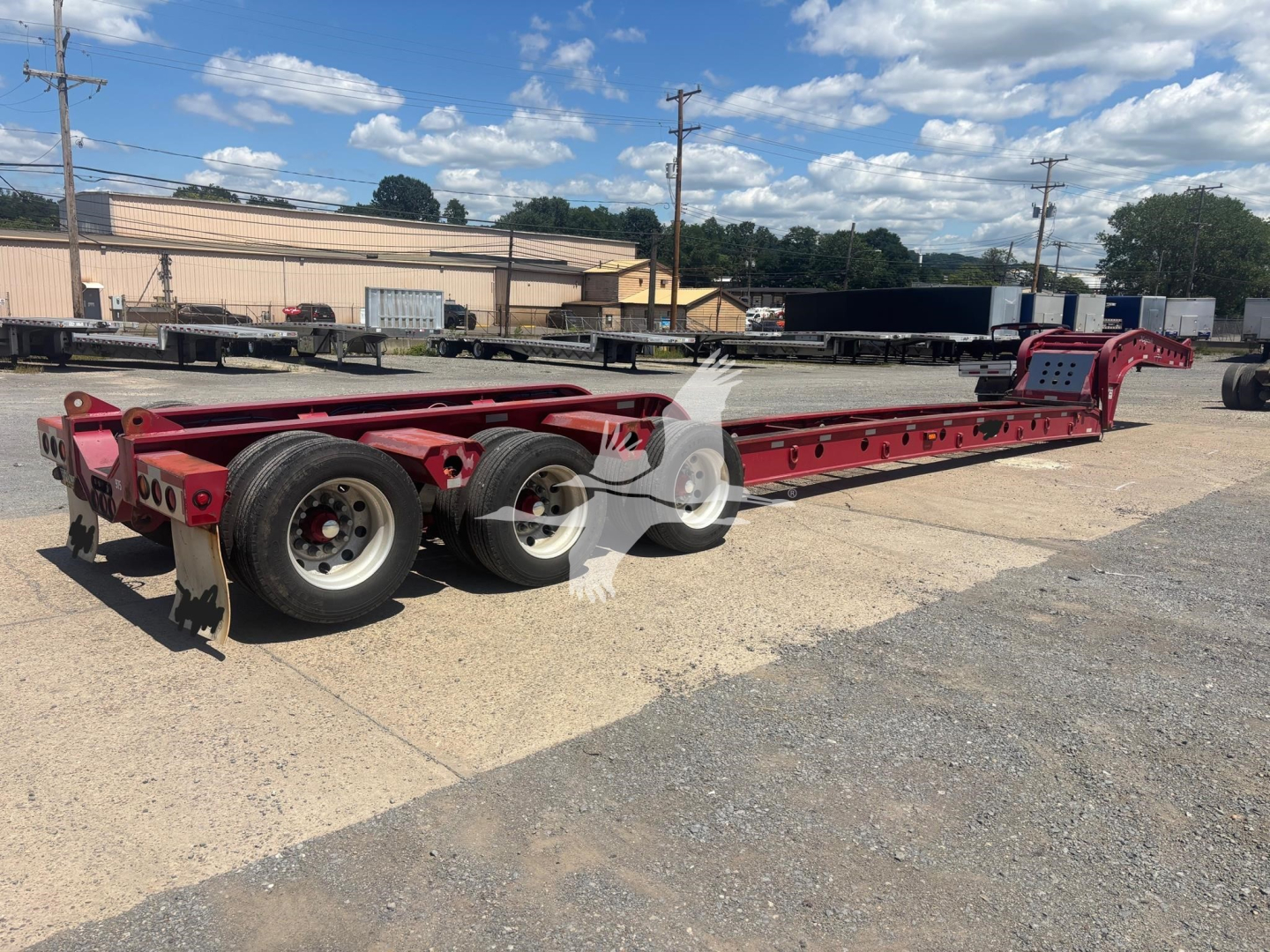 Long red Fontaine beam trailer in a yard, triple-axle lowboy with long flatbed and low gooseneck, multiple support rails and hydraulic gooseneck ramp.
