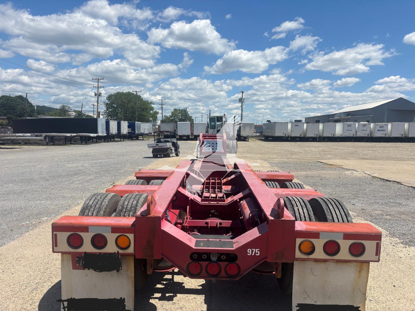 Rear view of a red Fontaine beam trailer chassis with dual rear axles, black tires, and multiple circular taillights and reflectors. Clear sky with clouds.