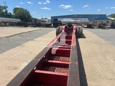 Beam trailer chassis showing red painted main frame with stepped chassis steps and dual rear axles in distance.