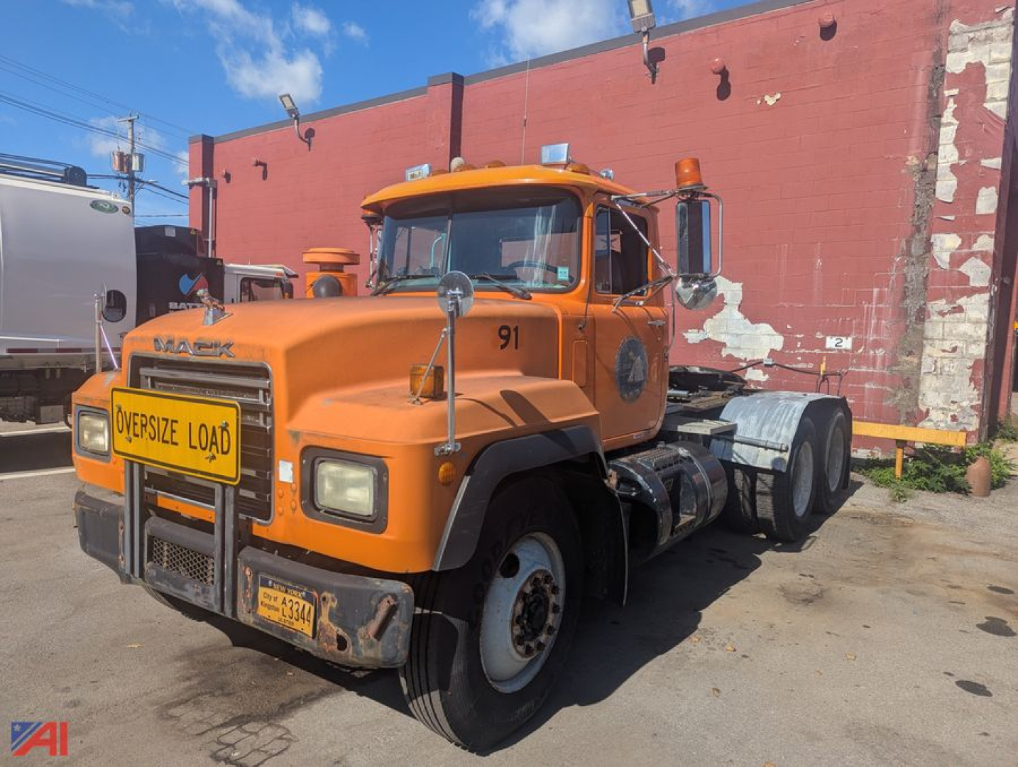 Mack RD6 tractor showing front view with orange cab and oversized load sign, grille guard, dual mirrors, and 3-axle configuration.