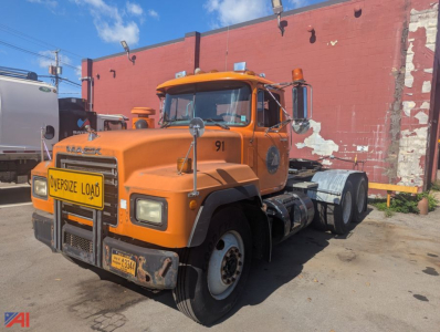 Mack RD6 tractor showing front view with orange cab and oversized load sign, grille guard, dual mirrors, and 3-axle configuration.