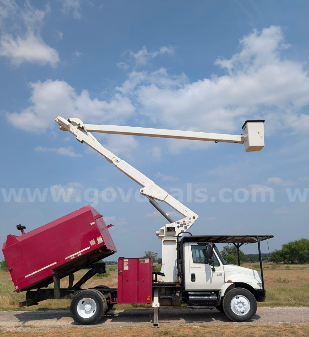 Truck-mounted boom lift with white cab and red dump bed raised on a hydraulic arm.
